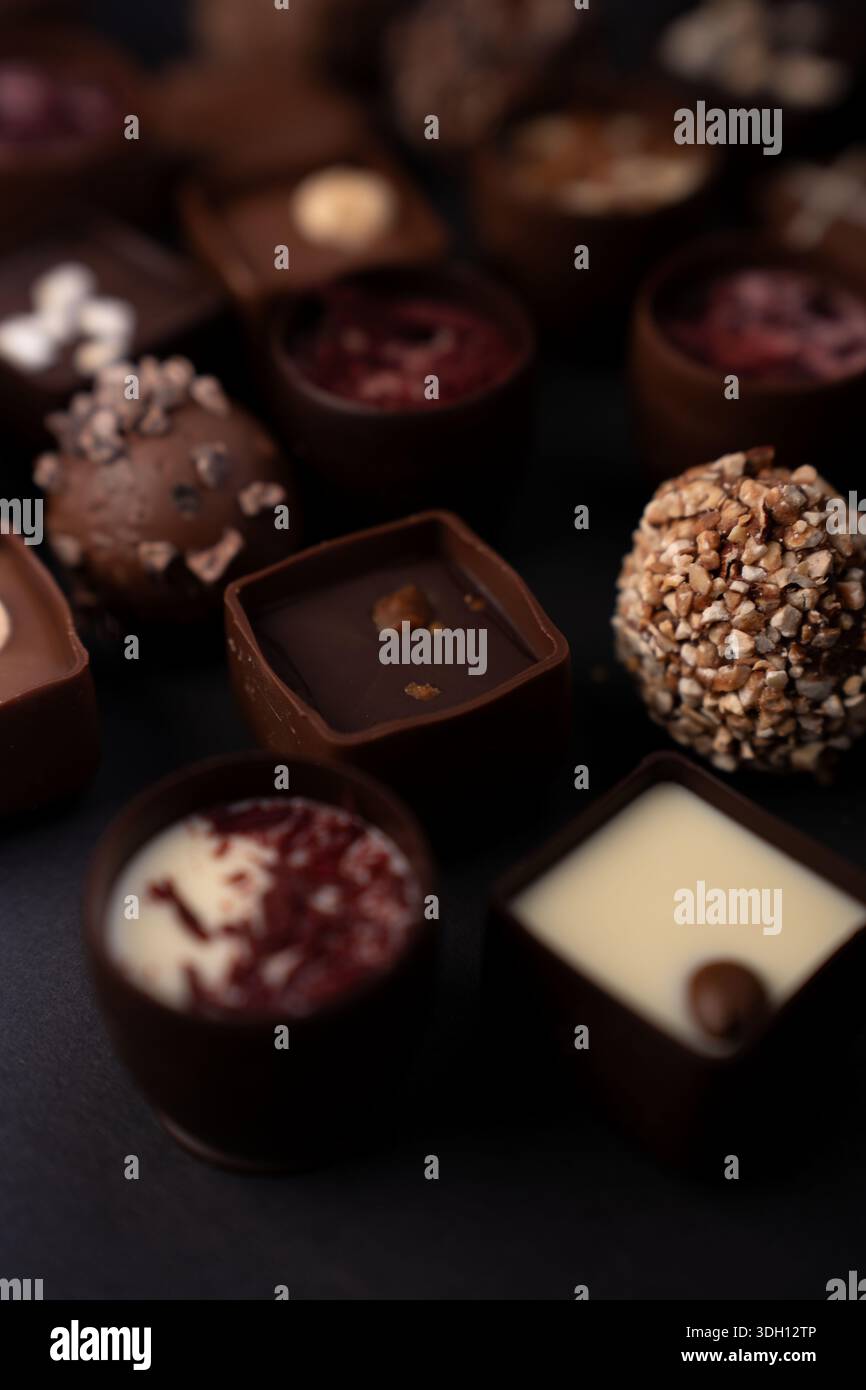 primo piano assortimento di tartufi e praline artigianali al cioccolato su un tavolo scuro, tonalità calde di marrone e cremose, ganache lucide e sfera ricoperta di noci Foto Stock