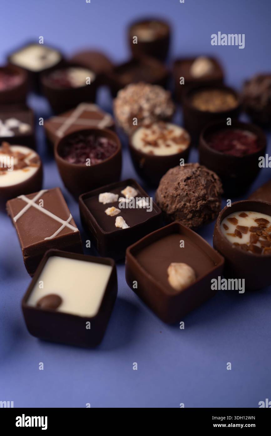 primo piano di praline e tartufi di cioccolato assortiti disposti su un tavolo blu, con ganaci scuri, latte e bianchi, farciture di nocciola, te Foto Stock