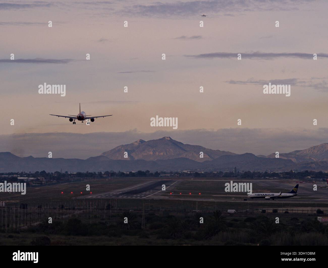 Aereo atterrando sul campo di volo dove un altro aereo è in attesa di decollo e terzo aereo che vola via ad altitudine Foto Stock