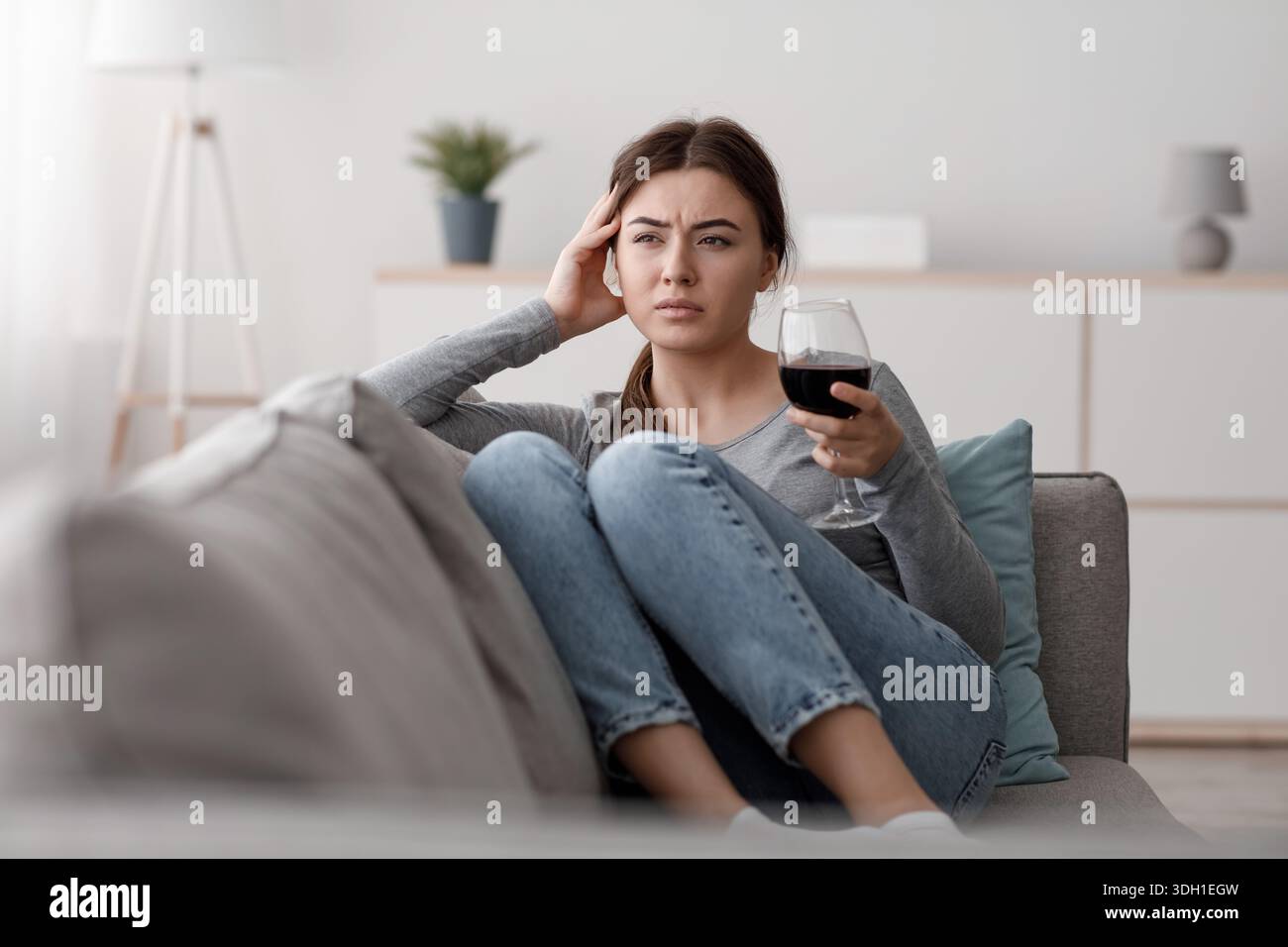 Triste frustrato giovane donna caucasica con un bicchiere di vino che soffre di depressione, stress e lavoro eccessivo a casa Foto Stock