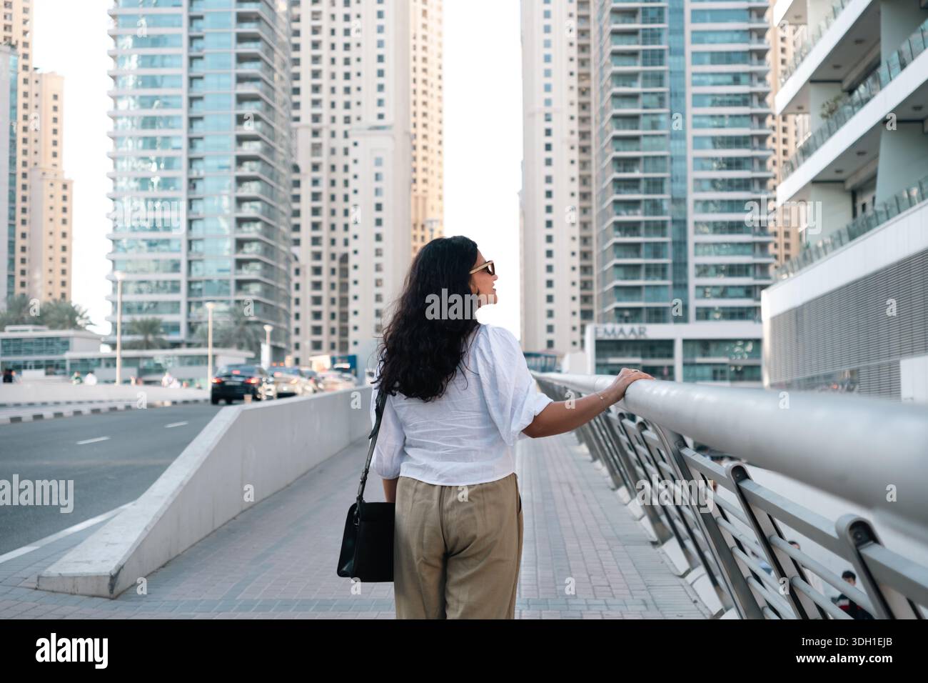 Viaggiatrice solitaria che cammina attraverso le moderne strade della Marina di Dubai con vista ad angolo basso Foto Stock