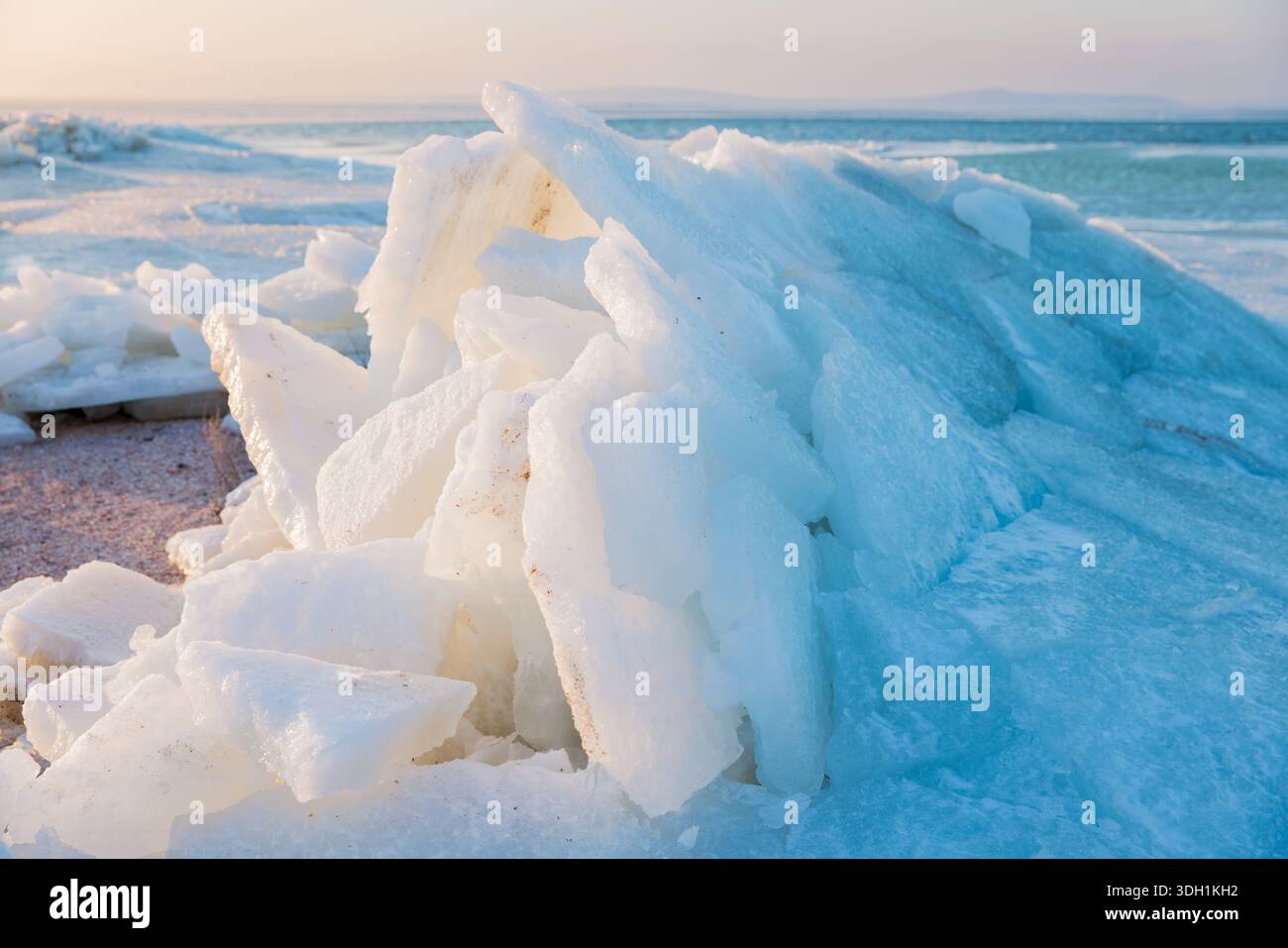Costa ghiacciata con lastre di ghiaccio impilate al tramonto, paesaggio invernale e strati cristallini spezzati. Foto Stock
