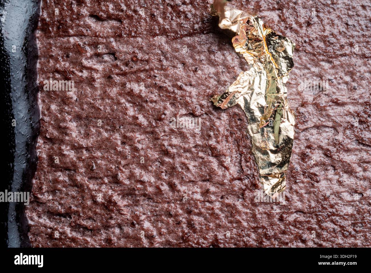 Primo piano di una ricca texture di crema di cioccolato decorata con brillanti accenti di foglie d'oro commestibili e ganache scure sul lato. Foto Stock