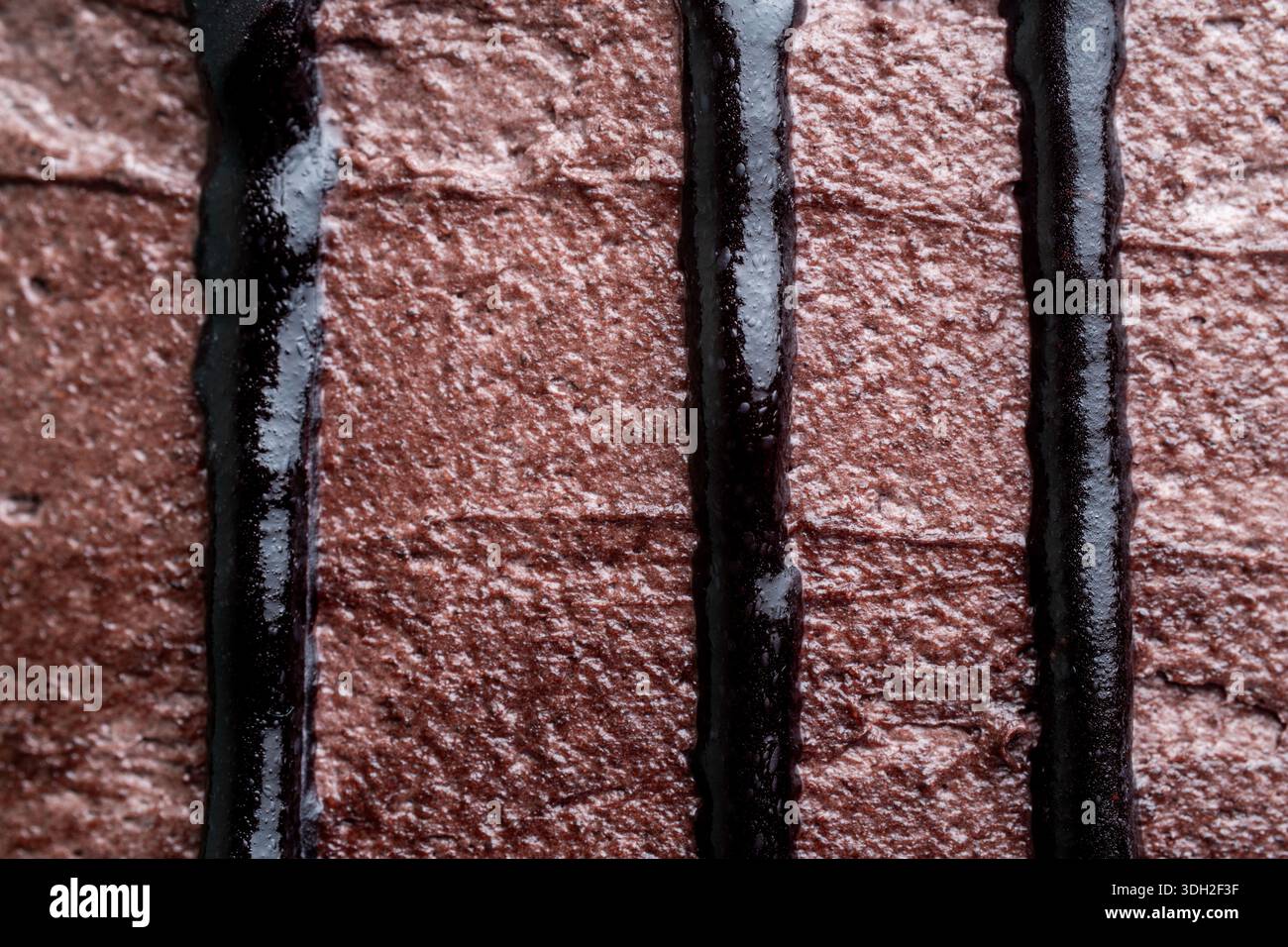 Primo piano di lucenti ganache al cioccolato fondente che gocciolano verticalmente su una torta con crema di burro di cacao, creando un delizioso motivo lineare. Foto Stock
