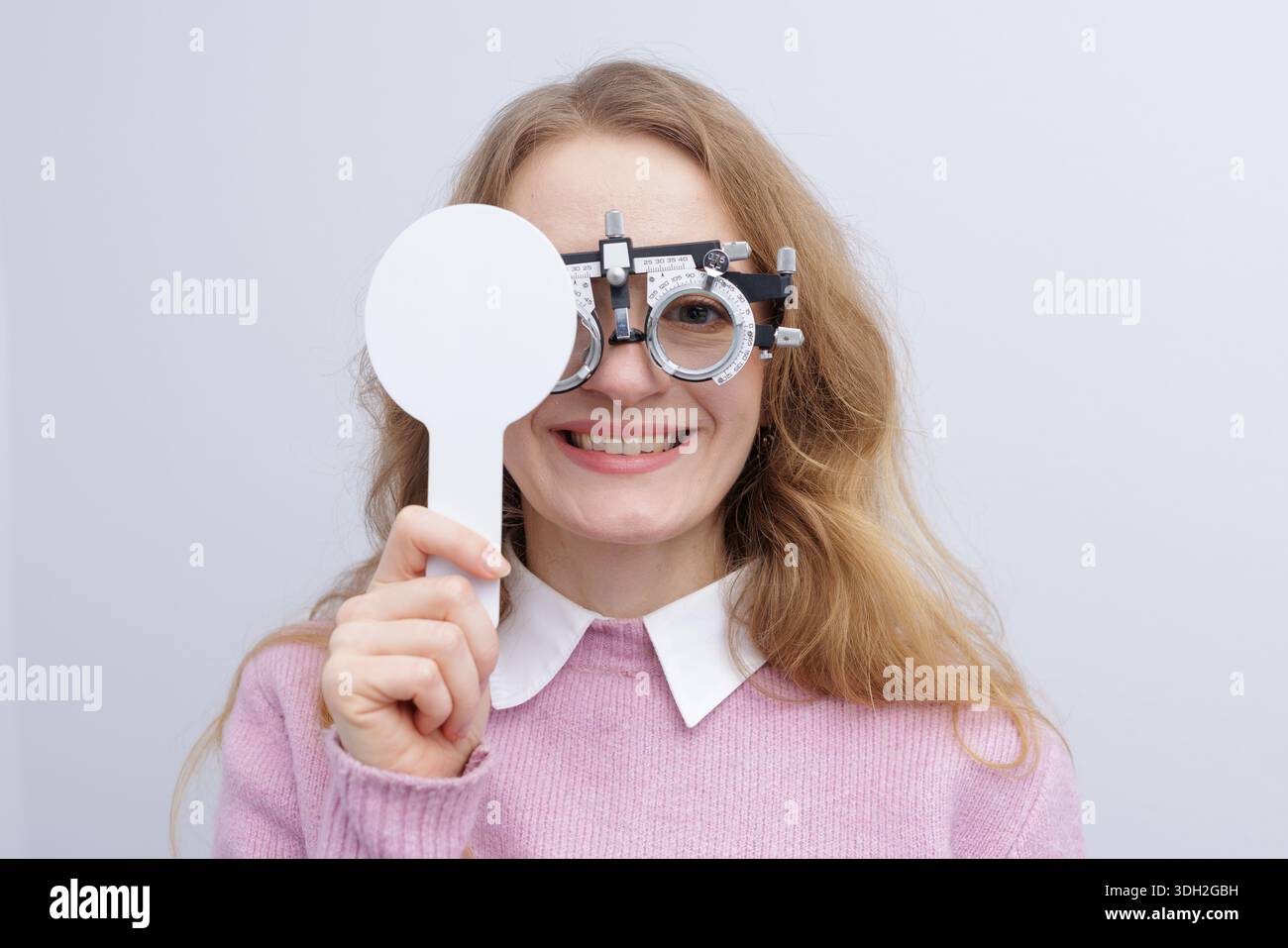 Il paziente sorridente nel telaio di prova copre un occhio con occlusivo durante l'esame di rifrazione. Ideale per siti web di cliniche oculistiche, brochure e annunci per la cura della vista. Foto Stock