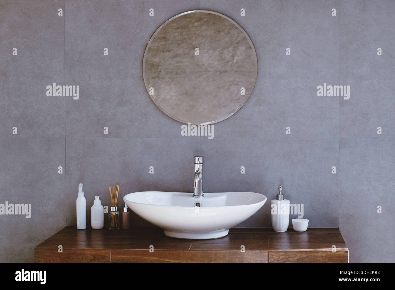 Bagno moderno con uno specchio rotondo e un lavandino bianco su un tavolo di legno Foto Stock