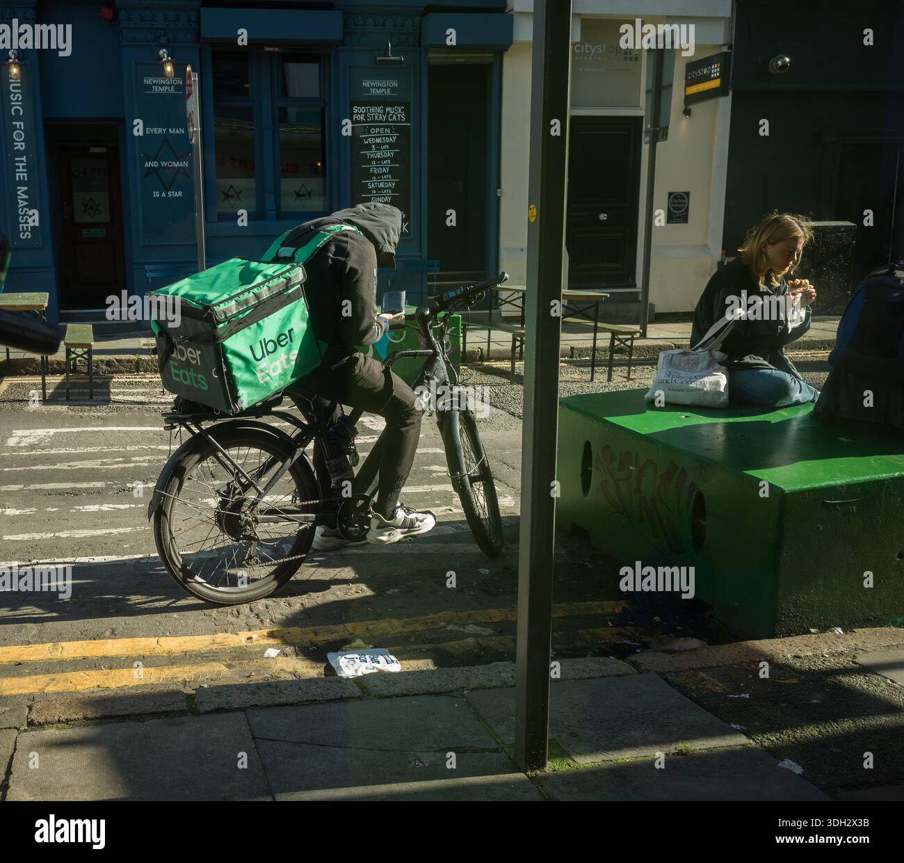 Un Uber Eats consegna fast food mette in pausa mentre guarda il suo telefono. Foto Stock
