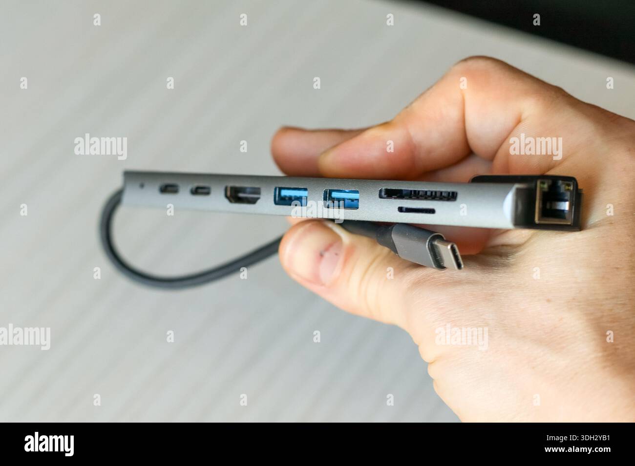 Foto dettagliata di una mano che tiene in mano un hub USB-C multifunzione grigio con porte Ethernet, USB e HDMI collegate tramite cavo Foto Stock