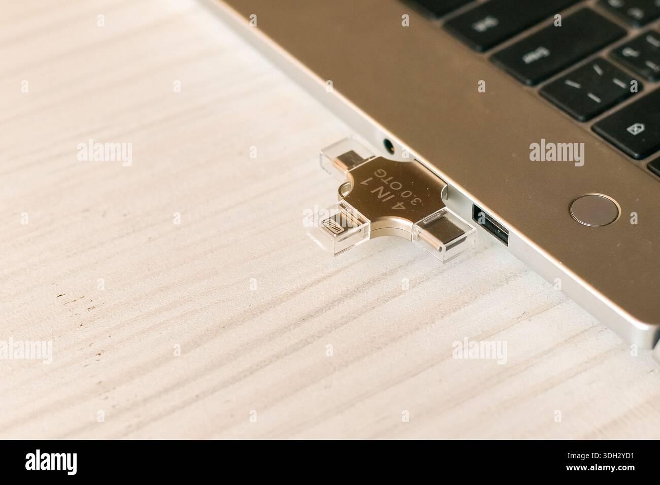 Angolo laterale di un sottile computer laptop color argento dotato di un'unità flash USB multi-connettore collegata su un tavolo in legno, ideale per la sincronizzazione dei dati tra dispositivi Foto Stock
