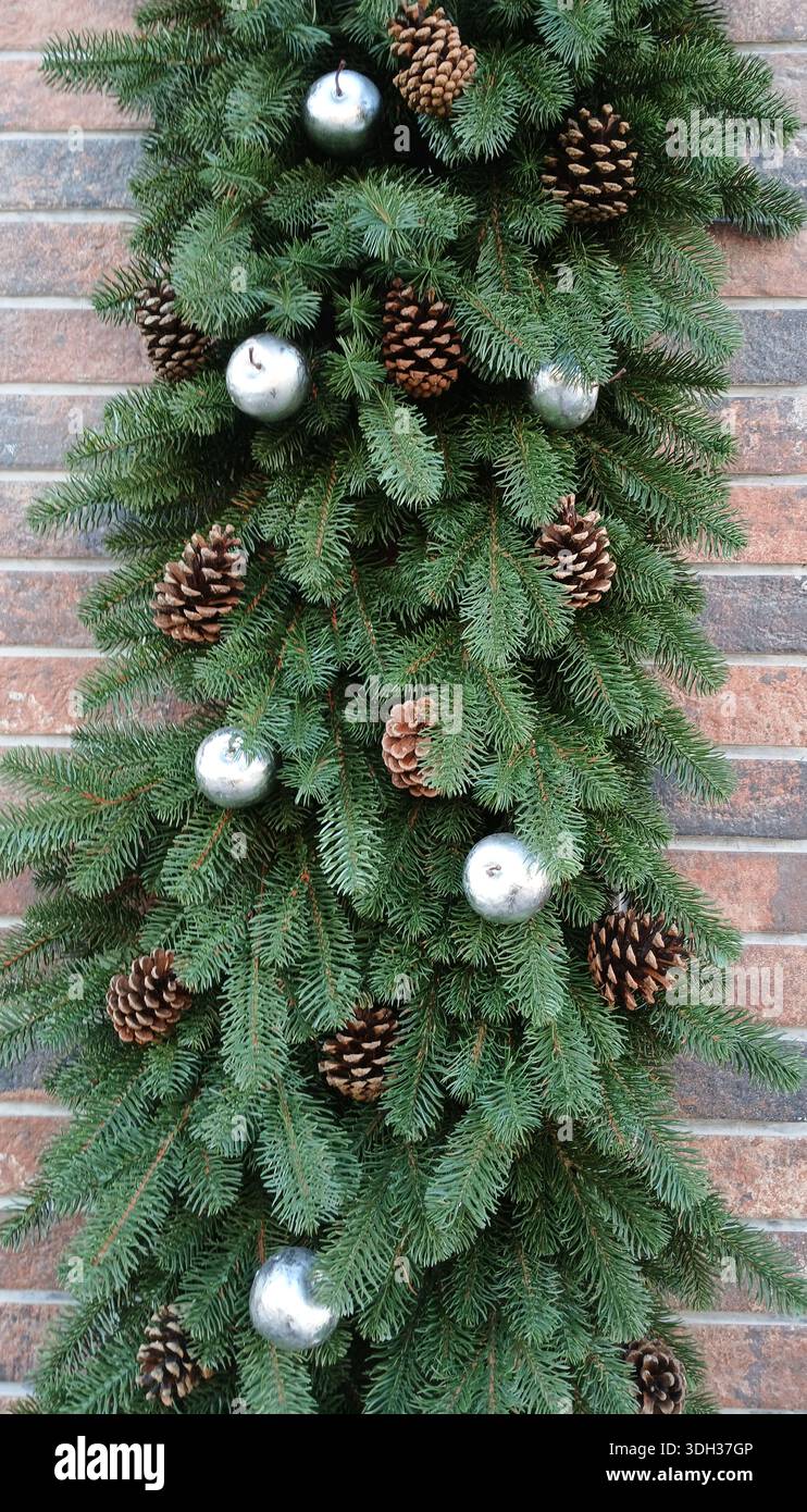 ghirlanda Evergreen con dettagli pinecone e palline d'argento su pareti in mattoni per un arredamento di festa Foto Stock