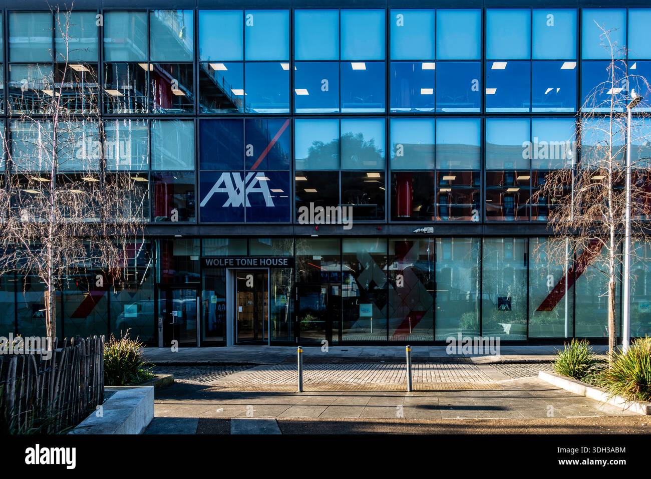 La moderna facciata in vetro della Wolfe Tone House di Dublino, con il famoso logo AXA, riflette la vita della città in una giornata vivace e luminosa. Foto Stock