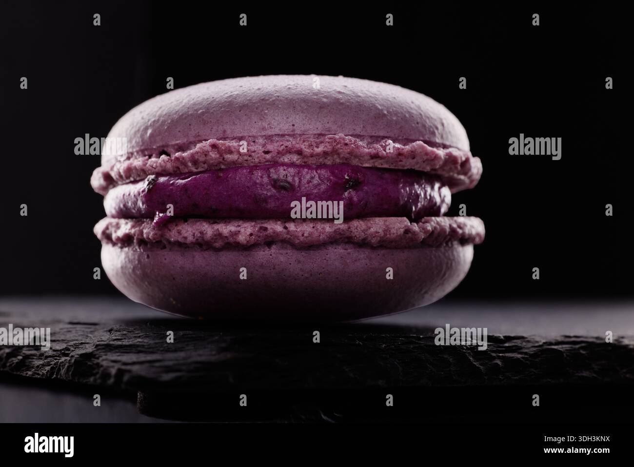 Macaron viola gustosi biscotti su sfondo nero. Dolce tradizionale francese, pasticceria gourmet Foto Stock