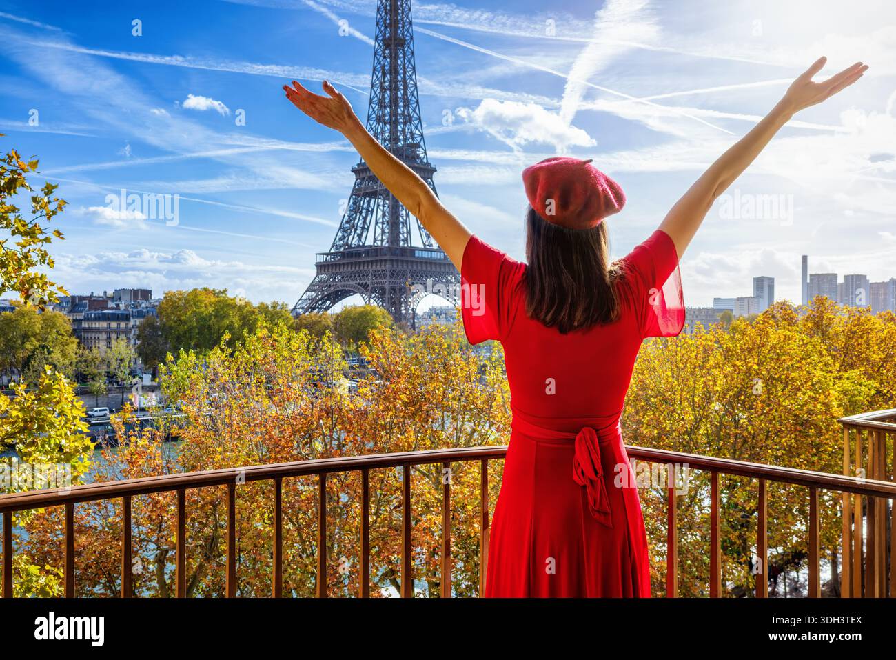 Una donna felice in un abito rosso che gode della vista dal suo balcone della Torre Eiffel e dello skyline di Parigi, in Francia, durante una giornata suny Foto Stock