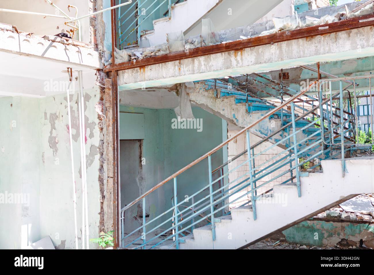 L'interno dell'edificio abbandonato mostra una scala in cemento in decomposizione con ringhiere in metallo blu e gravi danni strutturali. Rimozione della vernice e dei detriti Foto Stock