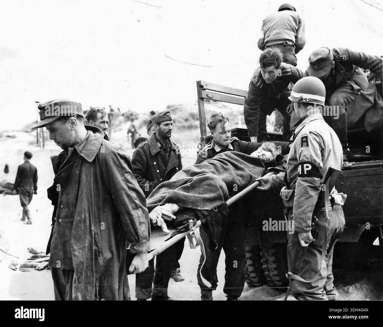 Prigionieri tedeschi scaricano compagni feriti su una spiaggia della Normandia dopo il D-Day. Il 6 giugno 1944 un'enorme forza d'invasione Alllied che coinvolgeva 7000 navi e 140.000 uomini sbarcò con successo sulla costa francese e stabilì cinque teste di spiaggia. Una campagna di inganno di successo significò che gran parte della resistenza tedesca si trovava a Calais e le perdite furono relativamente poche per le dimensioni e i rischi dell'operazione. Foto Stock