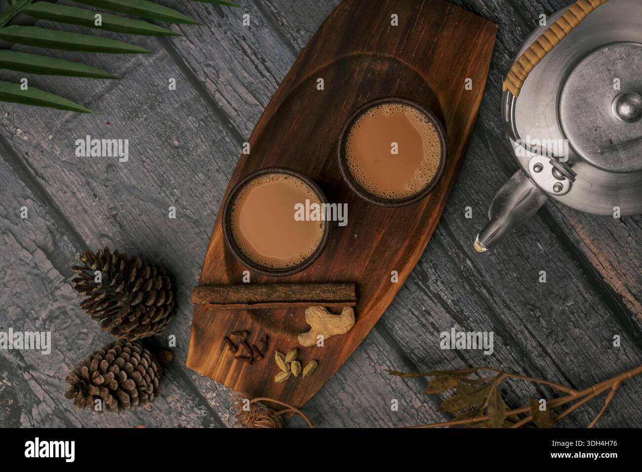 Un vassoio di legno con due tazze di tè e un bollitore per tè è collocato su un tavolo di legno. Il vassoio è decorato con bastoncini di cannella e zenzero, dandogli un tocco Foto Stock