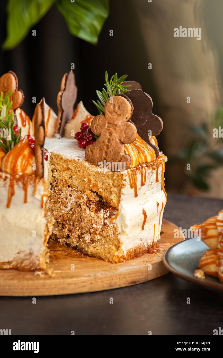 Una torta a strati speziata festosa decorata con biscotti man pan di zenzero, rosmarino e ribes rossi, caratterizzata da un gocciolamento di caramello dorato. Foto Stock