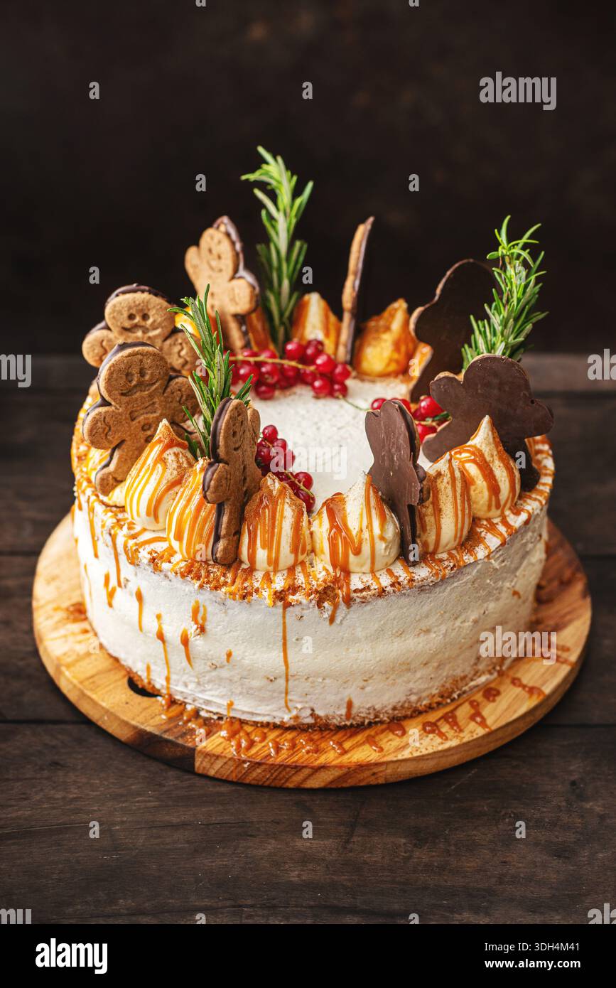 Una torta a strati speziata festosa decorata con biscotti man pan di zenzero, rosmarino e ribes rossi, caratterizzata da un gocciolamento di caramello dorato e una cremosa gelata bianca. Foto Stock