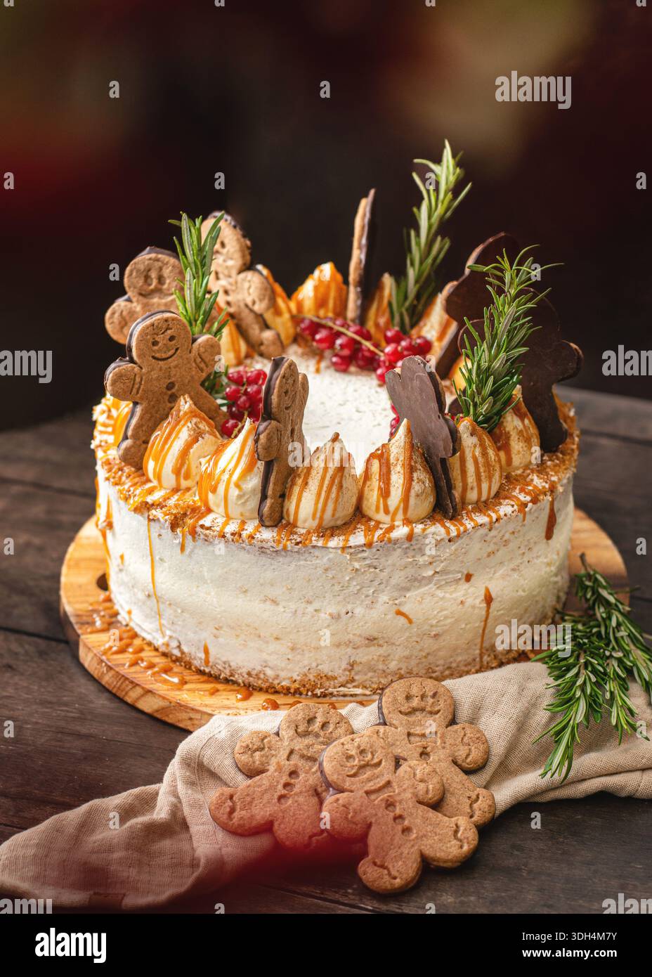 Una torta a strati speziata festosa decorata con biscotti man pan di zenzero, rosmarino e ribes rossi, caratterizzata da un gocciolamento di caramello dorato e una cremosa gelata bianca. Foto Stock