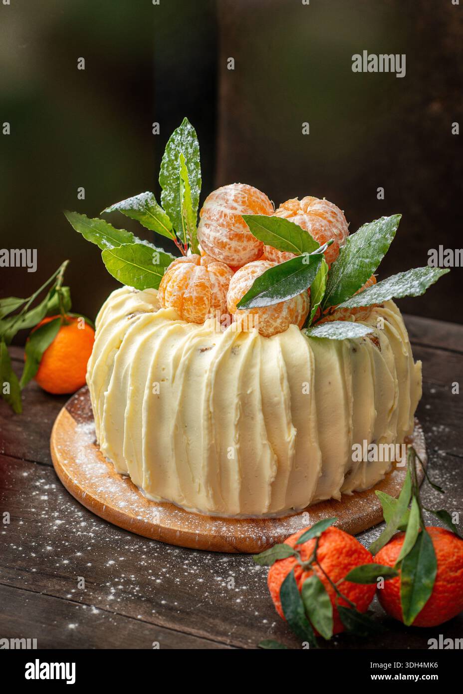 Una torta di spugne festosa decorata con mandarini interi freschi e foglie verdi, con spessa glassa di crema bianca. Foto Stock