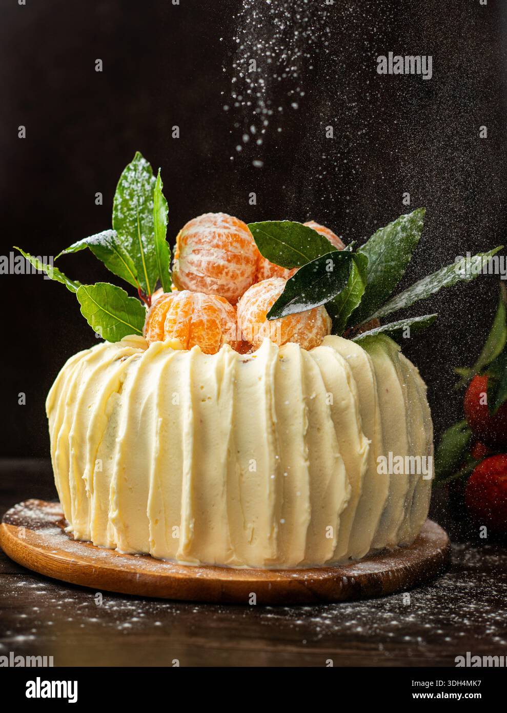 Una torta di spugne festosa decorata con mandarini interi freschi e foglie verdi, con spessa glassa di crema bianca. Foto Stock