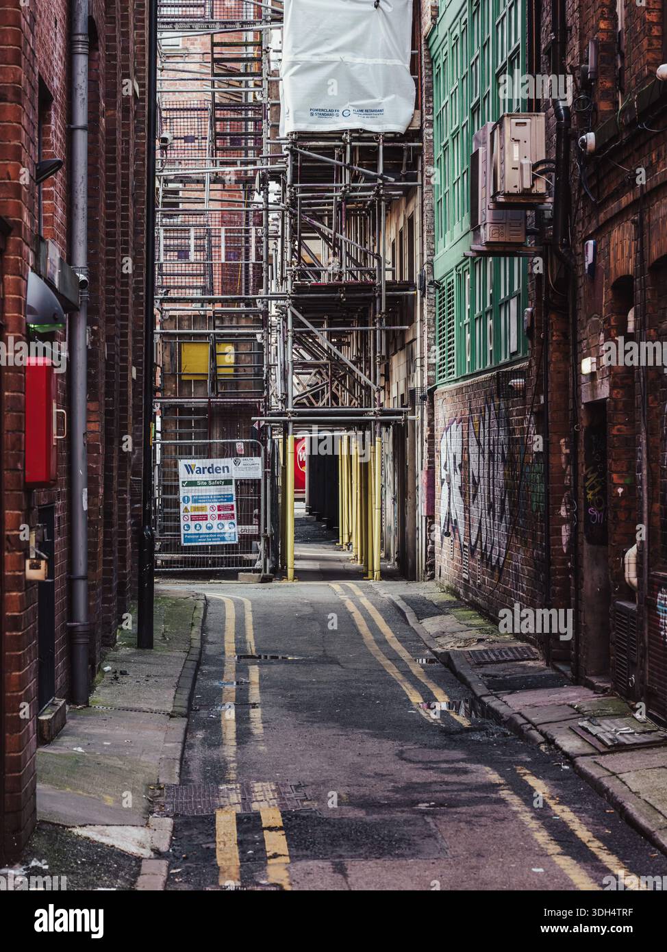 Manchester, Inghilterra, Marc h 04, 2024: Vicolo vuoto della città fiancheggiato da pareti in mattoni, ponteggi e superfici stradali usurate. Atmosfera urbana grintosa Foto Stock