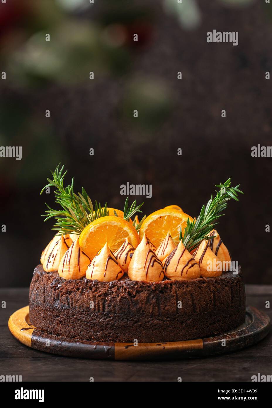 Una ricca torta al cioccolato ricoperta da vortici di meringa color arancio conditi con cioccolato, decorata con fette di arancia fresca e rametti di rosmarino. Foto Stock