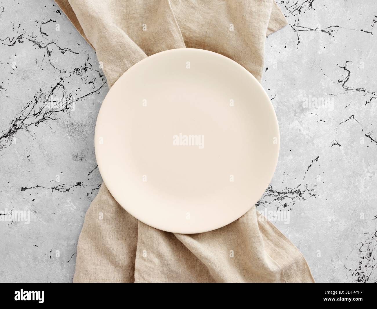 Piatto rotondo vuoto con tovagliolo di lino beige su un tavolo di marmo grigio, creando un ambiente minimalista e piatto Foto Stock