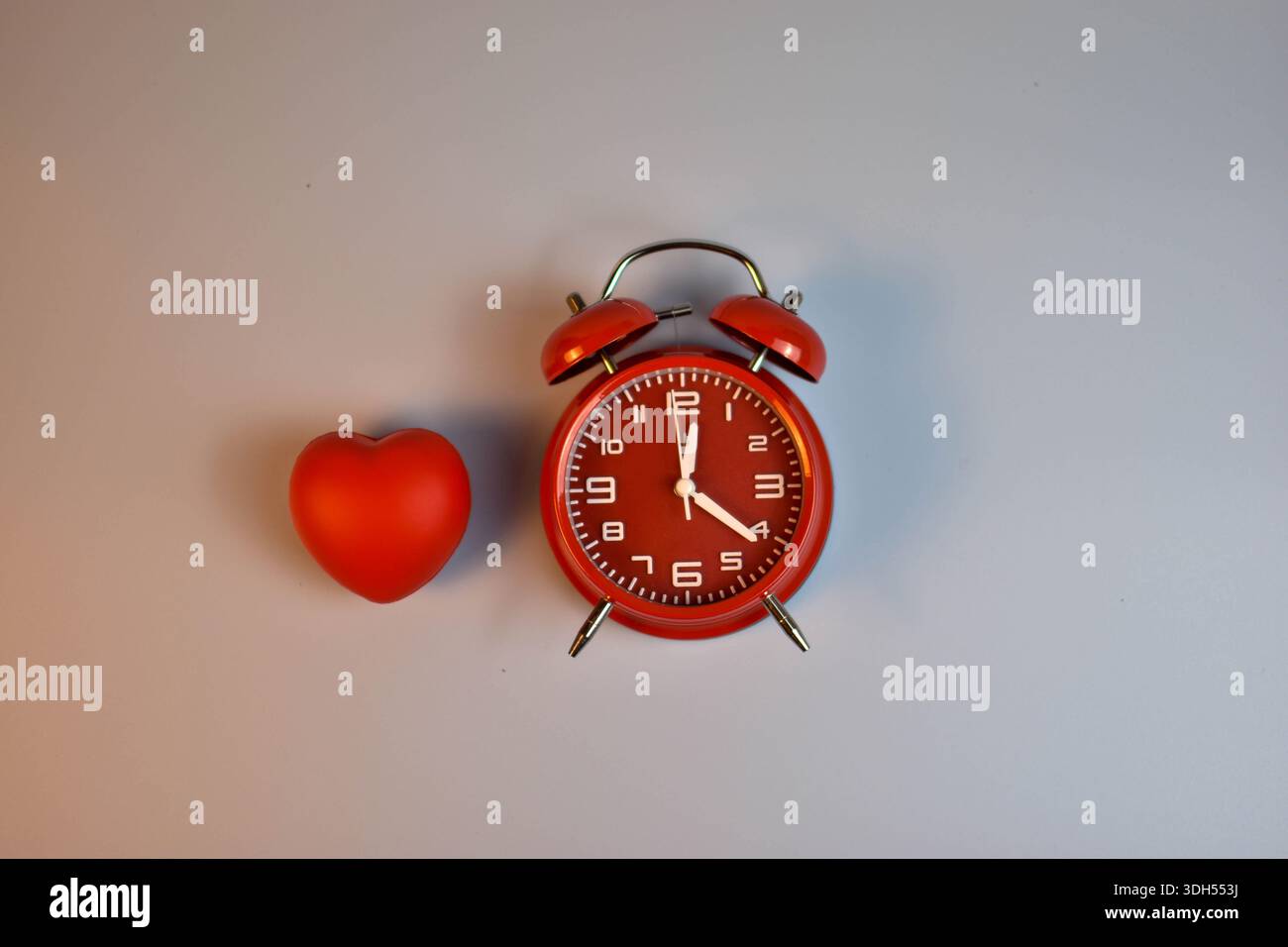 Cuore rosso e sveglia nera su abbinamento simbolico blu che suggerisce la connessione dell'amore con il tempo, l'urgenza o la presenza emotiva duratura. Foto Stock