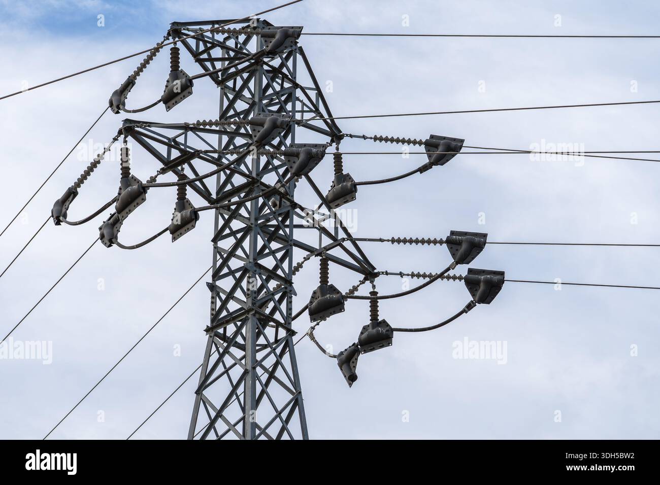Una vista dettagliata ad angolo basso di una torre di trasmissione elettrica ad alta tensione con più linee di alimentazione in contrasto con un cielo nuvoloso, che rappresenta l'energia Foto Stock