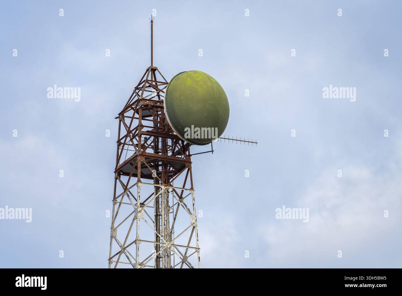 Un'alta torre di comunicazione satellitare con una caratteristica parabola verde si erge su un cielo azzurro e cristallino, mostrando tecnologia e infrastrutture di telecomunicazioni Foto Stock
