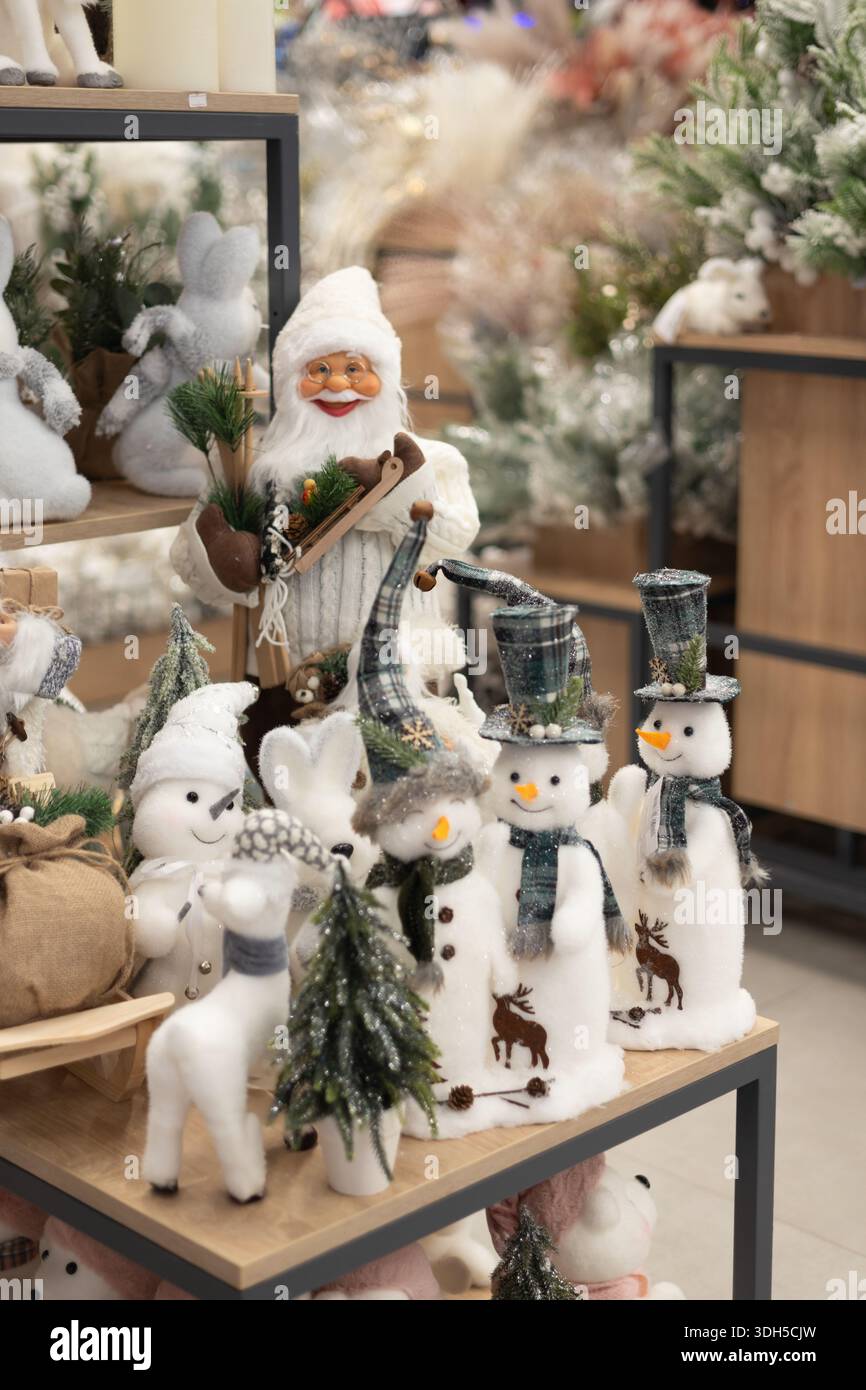 Un vivace negozio di giocattoli natalizi presenta lussuosi pupazzi di neve con cappelli e sciarpe a motivi geometrici, un'allegra statuetta di Babbo Natale e alberi decorativi su legno Foto Stock