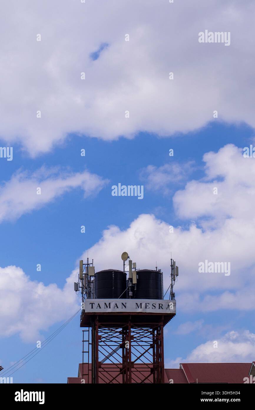 Sabah, Malesia - 18 gennaio 2026: Un'alta struttura a torre d'acqua vicino ad aree abitative con doppi serbatoi neri, antenne e parabole satellitari aga Foto Stock