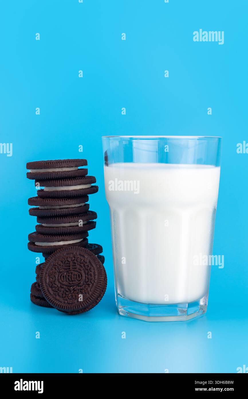 Horishni PlavniUkraine - 21 agosto 2022: Biscotti OREO in pila con un bicchiere di latte fresco su sfondo blu (famosa marca americana di biscotti) Foto Stock