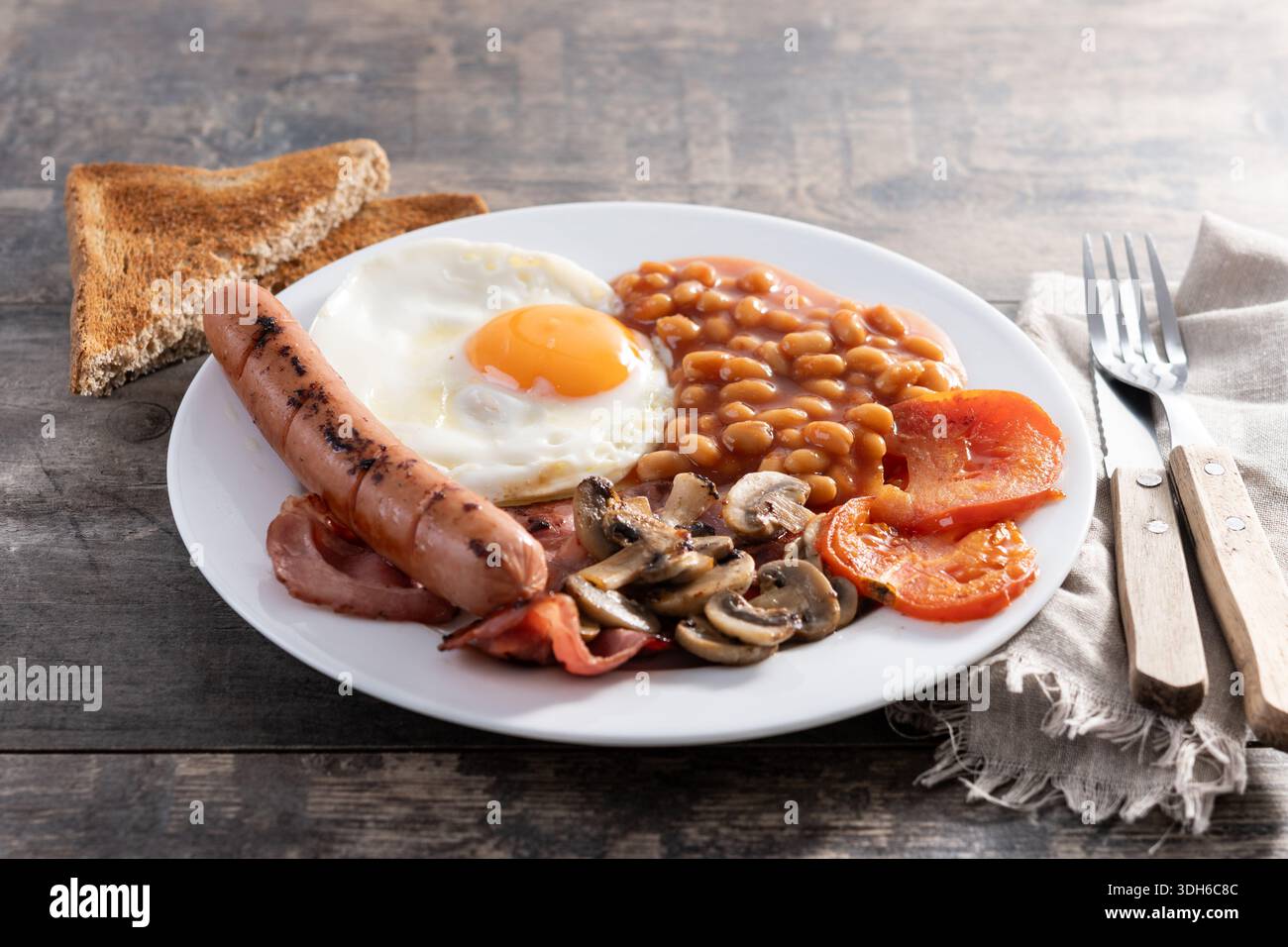 Colazione all'inglese completa con uova fritte, pancetta, salsicce e fagioli su un tavolo di legno Foto Stock
