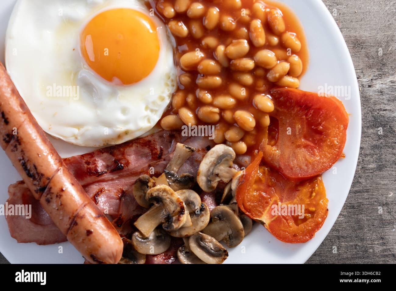 Colazione all'inglese completa con uova fritte, pancetta, salsicce e fagioli su un tavolo di legno Foto Stock