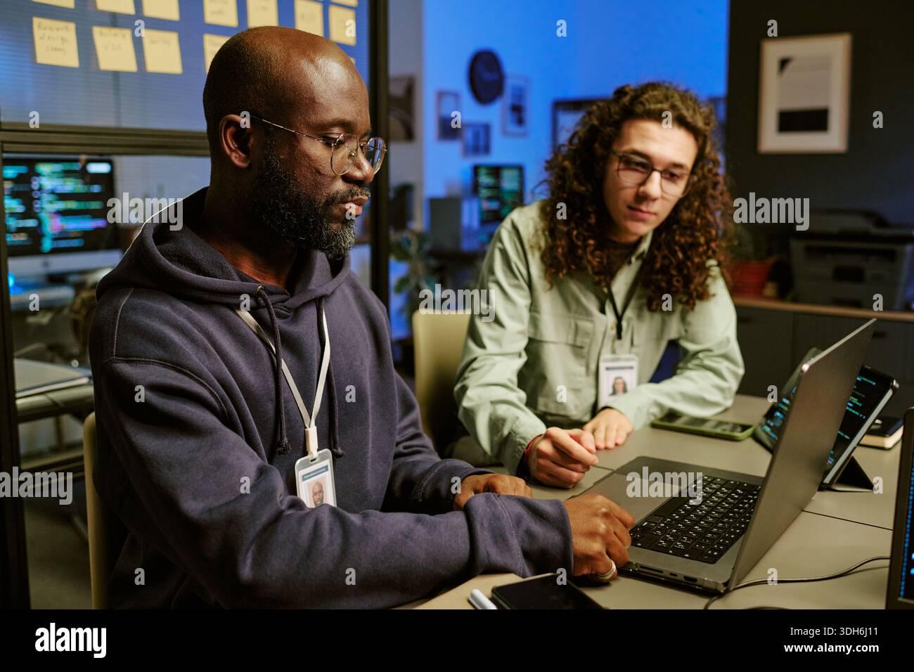 Giovane uomo nero e giovane uomo caucasico che collaborano su un laptop in ufficio Foto Stock