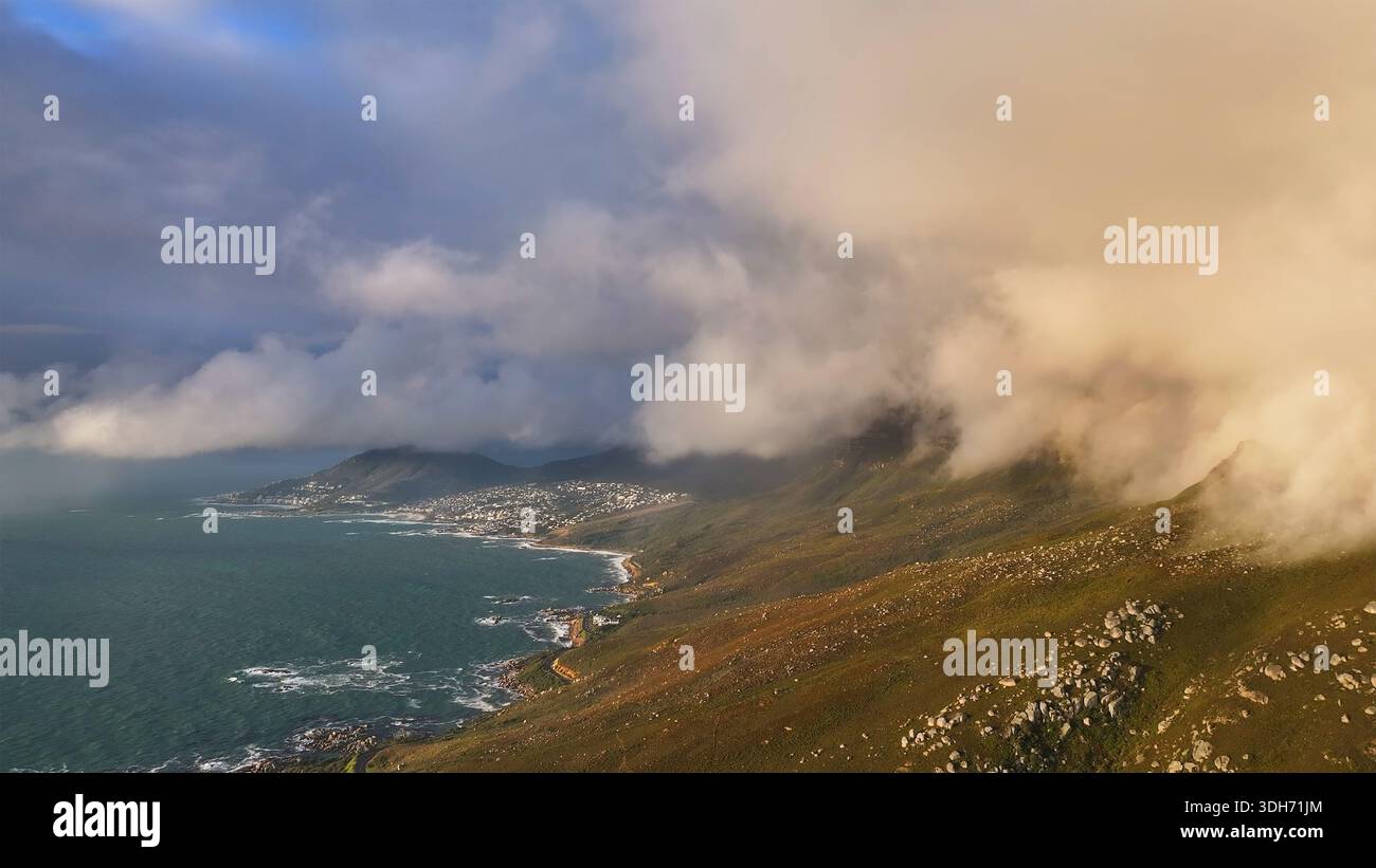 Vista aerea di spettacolari nuvole aggrappate alla costa frastagliata vicino a Camps Bay, dove l'oceano turchese incontra le colline dorate, città del Capo, Western C. Foto Stock