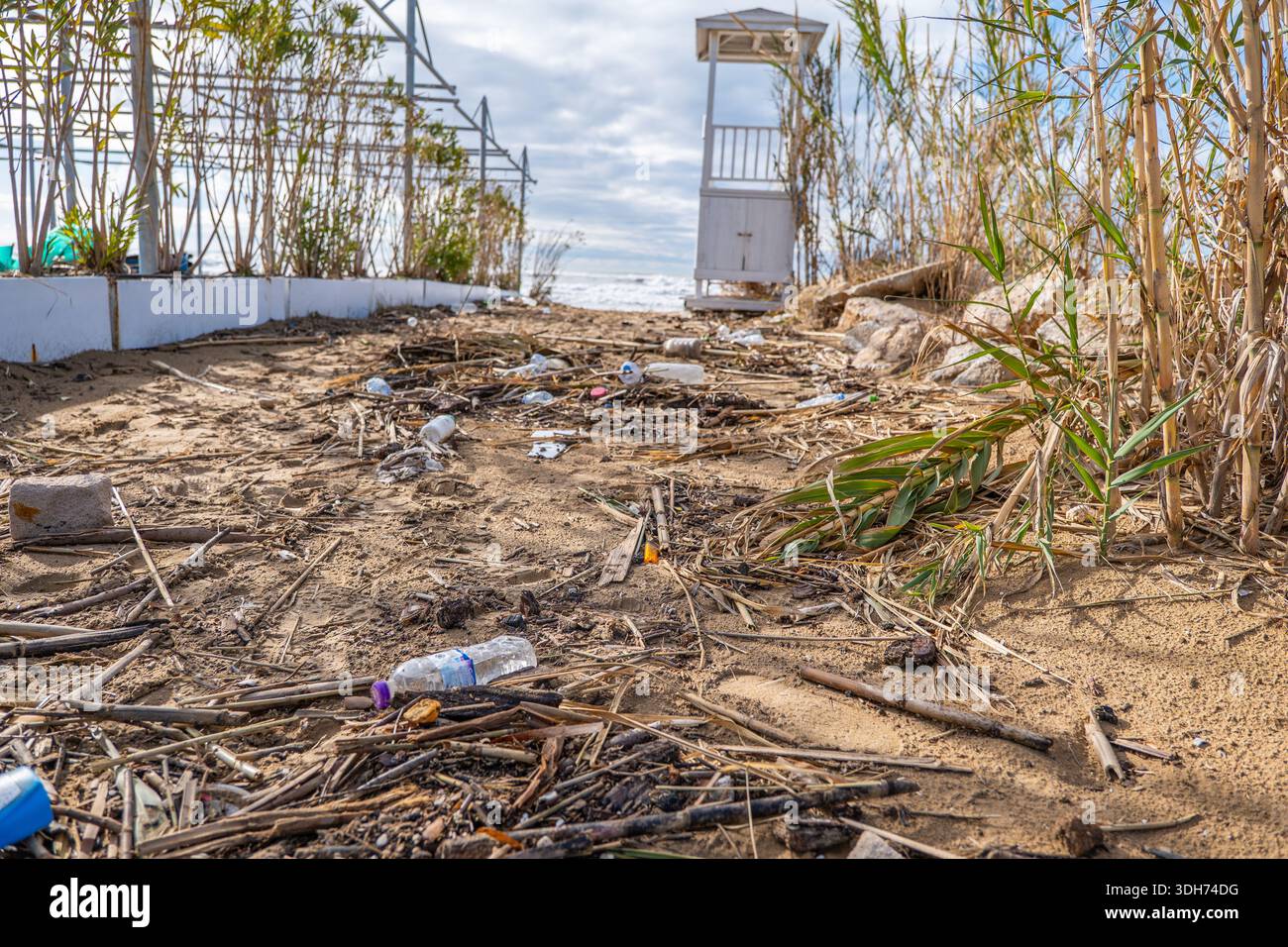 Inquinamento ambientale che mostra bottiglie di plastica e spazzatura sparsi tra le canne su una spiaggia sabbiosa vicino a una torre di bagnino. Foto Stock