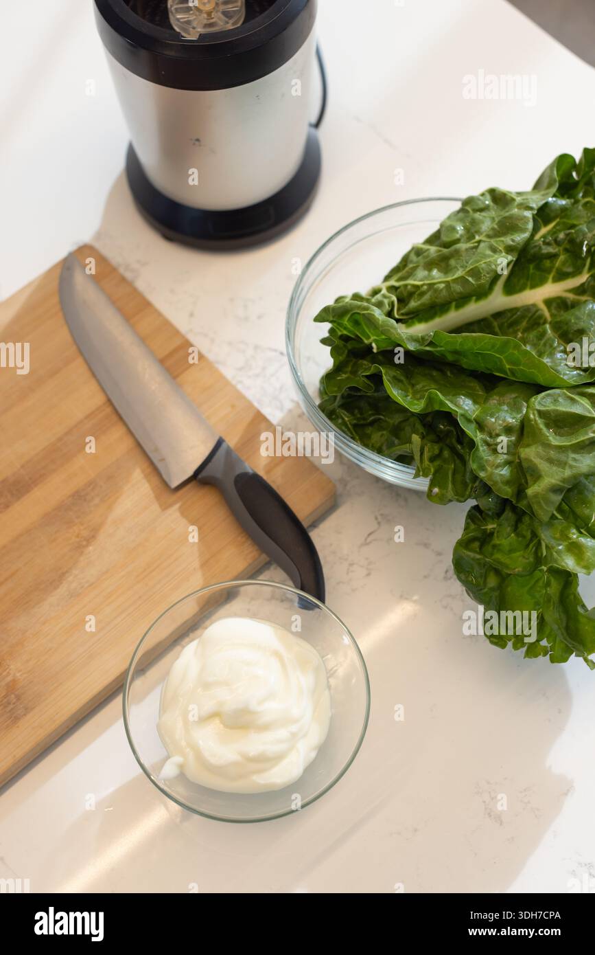 Un'ampia ciotola di verdure fresche si trova sul piano di lavoro in quarzo con tagliere, coltello, ciotola panna Foto Stock