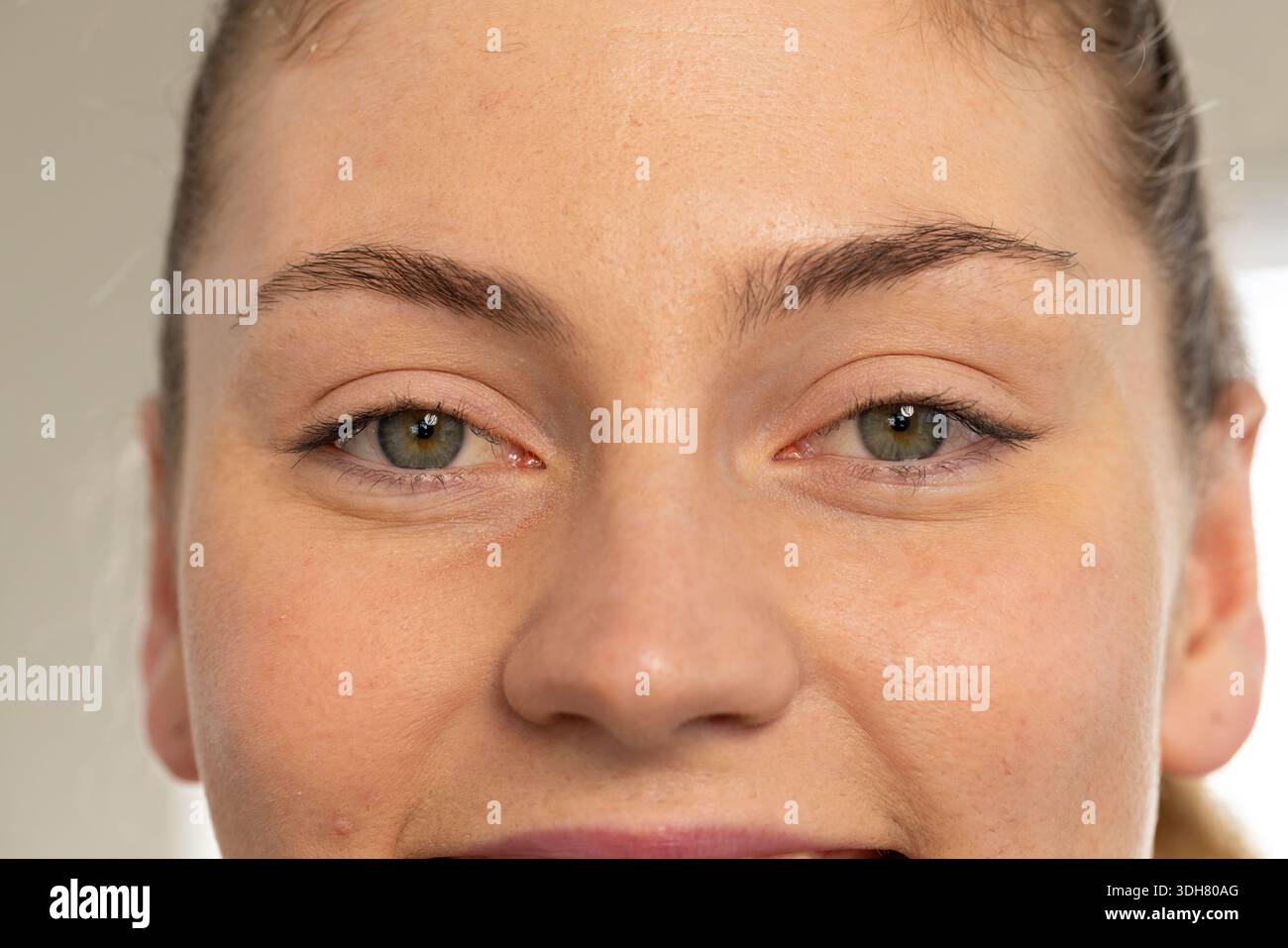 Fotocamera rivolta verso la donna, che sorride leggermente a bocca chiusa nella stanza, mostrando la consistenza della pelle e la luce del momento Foto Stock