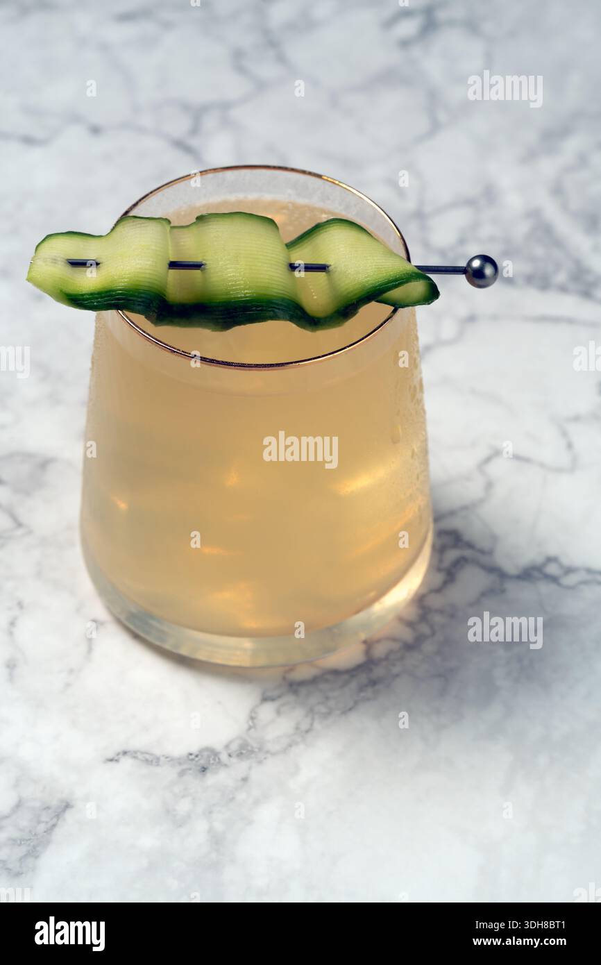 Vista dall'alto verso il basso di un cocktail giallo con nastro di cetrioli decorato su marmo. Rifrazione artistica della luce e ombre. Moderna estetica mixology Foto Stock