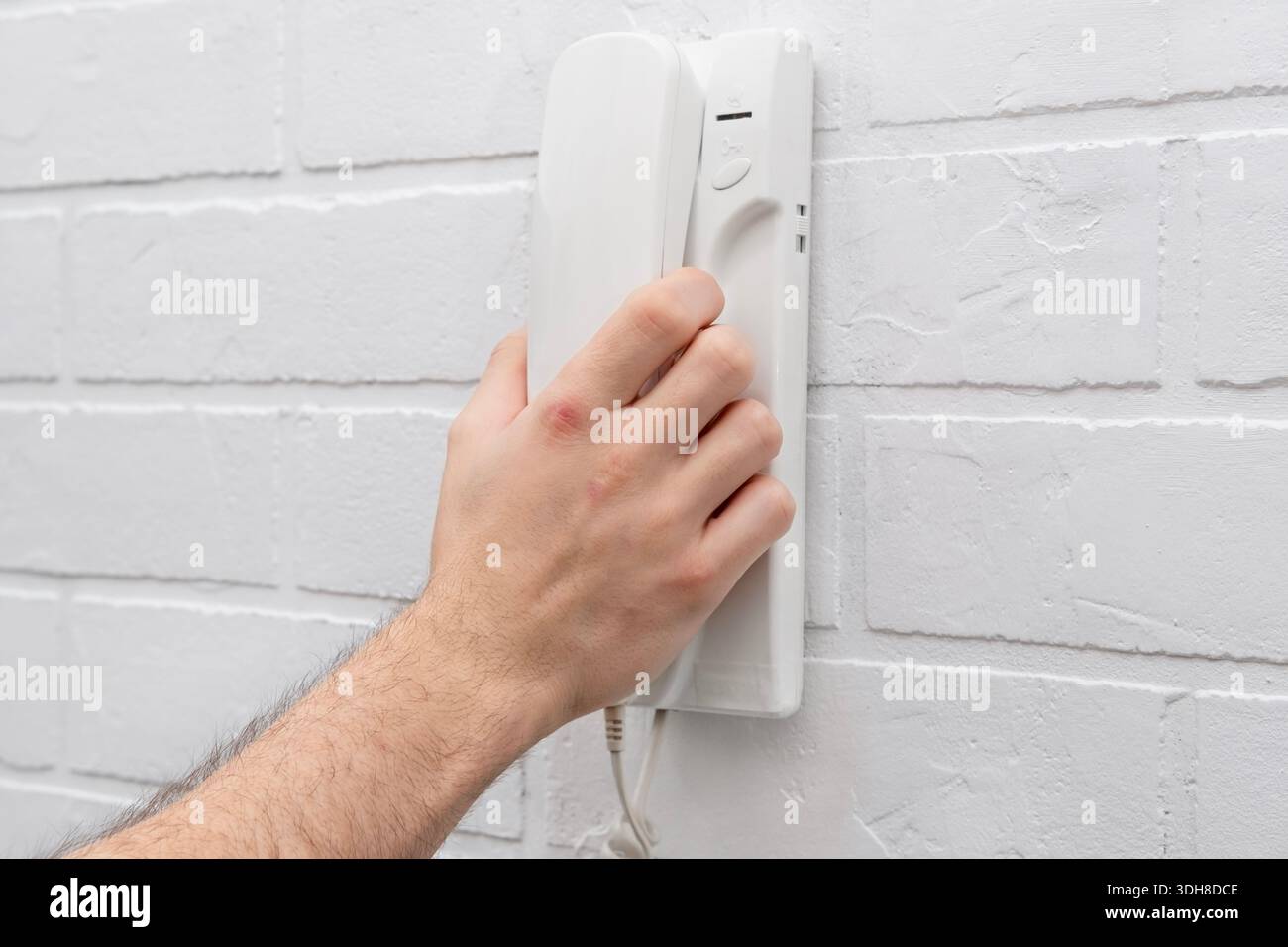 La mano di un uomo solleva un telefono interfono bianco. Foto Stock