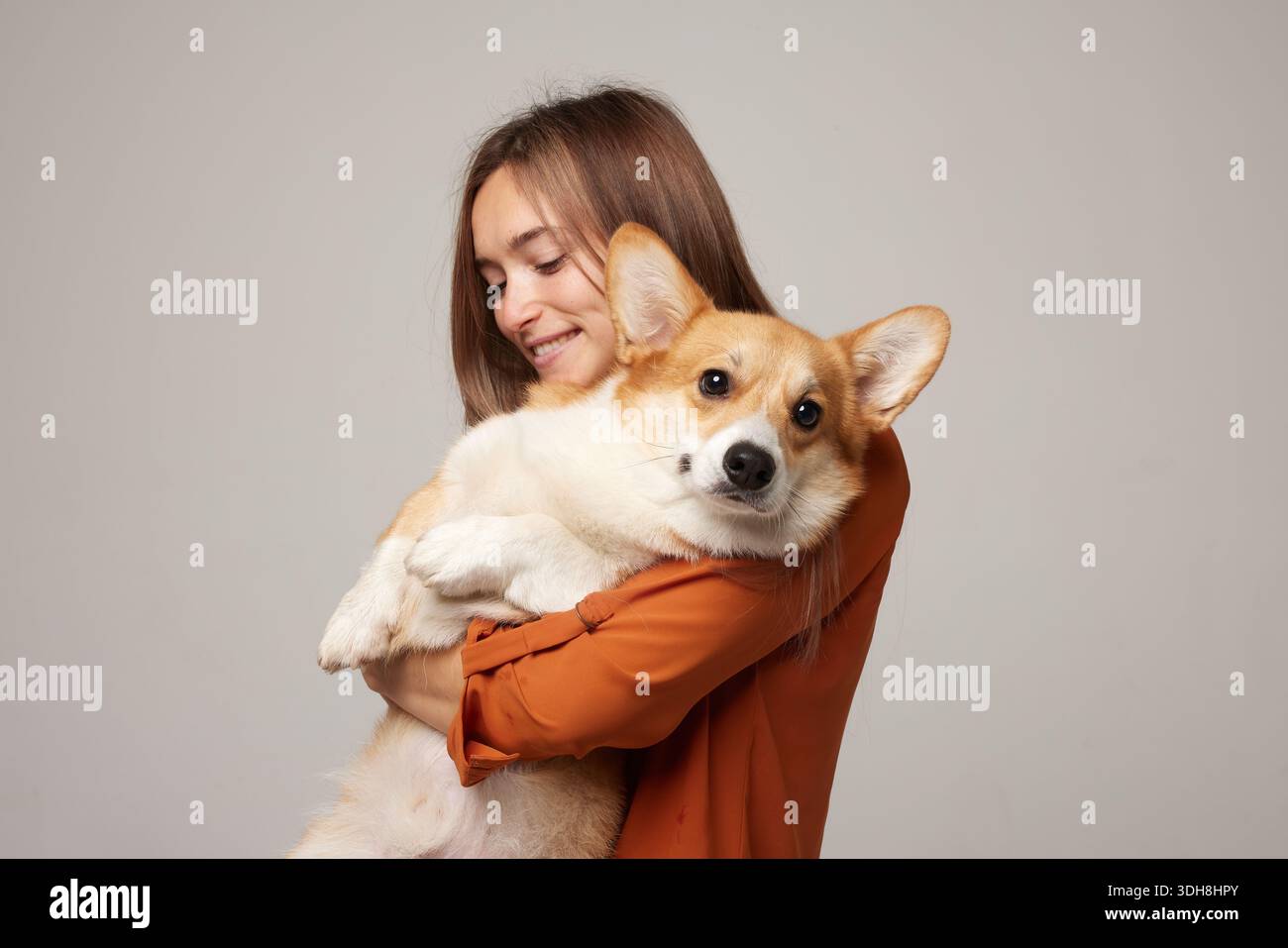 Ritratto in studio di una donna felice che coccola un cane corgi che guarda la macchina fotografica mostrando il comfort della compagnia e la cura responsabile del cane Foto Stock