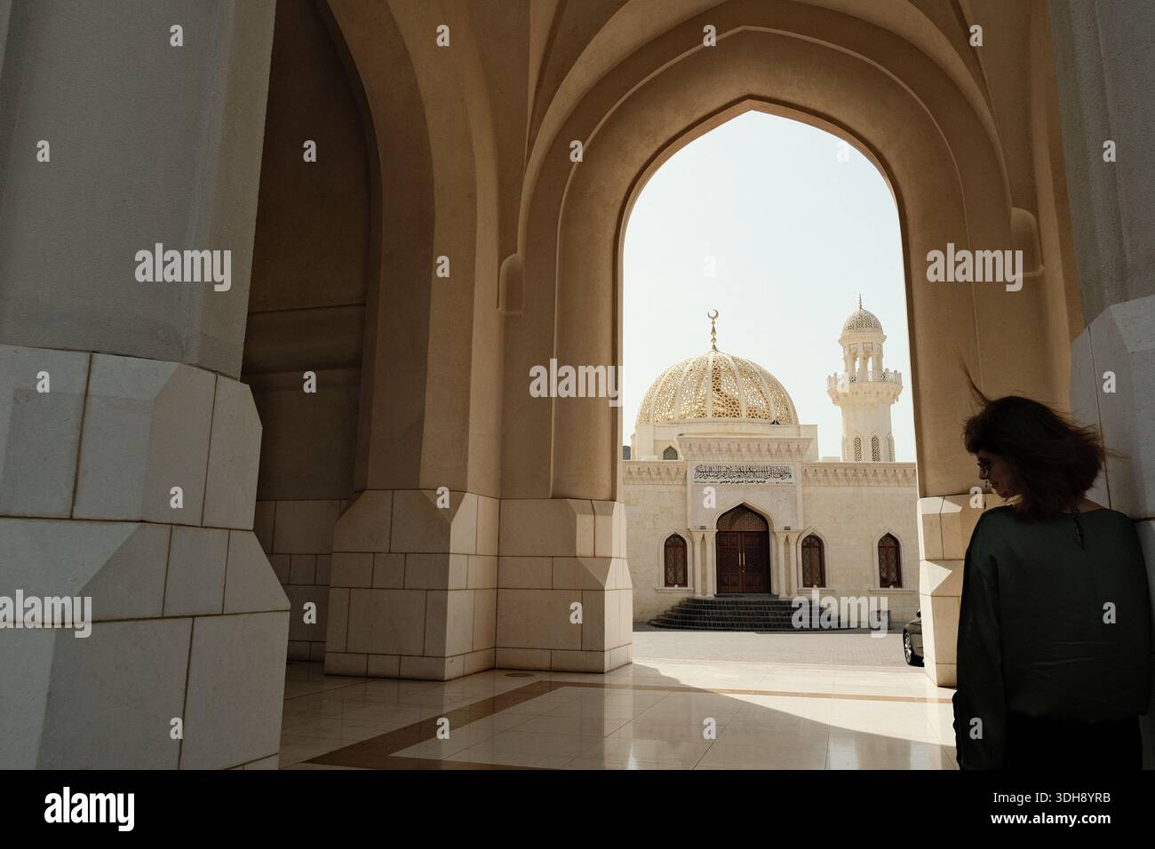 Donna che guarda il cortile attraverso un arco alla grande Moschea del Sultano Qaboos, Mascate, Oman Foto Stock