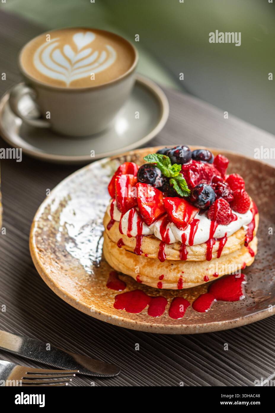 Frittelle di bacche fresche ricoperte di panna montata e servite su un piatto rustico insieme a un caffè di latte art. Deliziosa colazione o brunch. Foto Stock