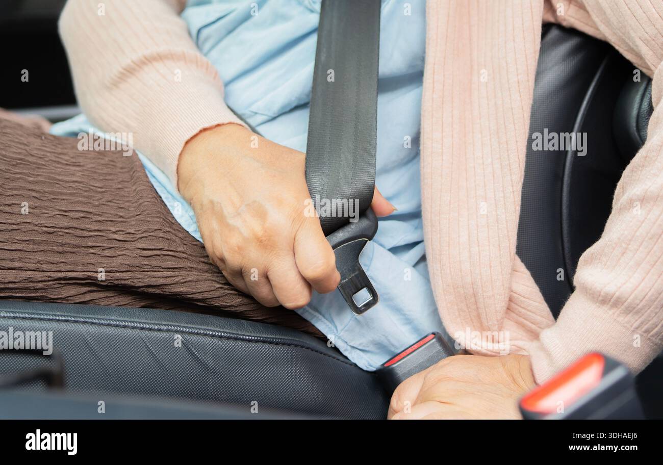 Primi piani di una donna matura che indossa la cintura di sicurezza. Allacciare la cintura di sicurezza nella vettura. Donna anziana che guida un'auto Foto Stock
