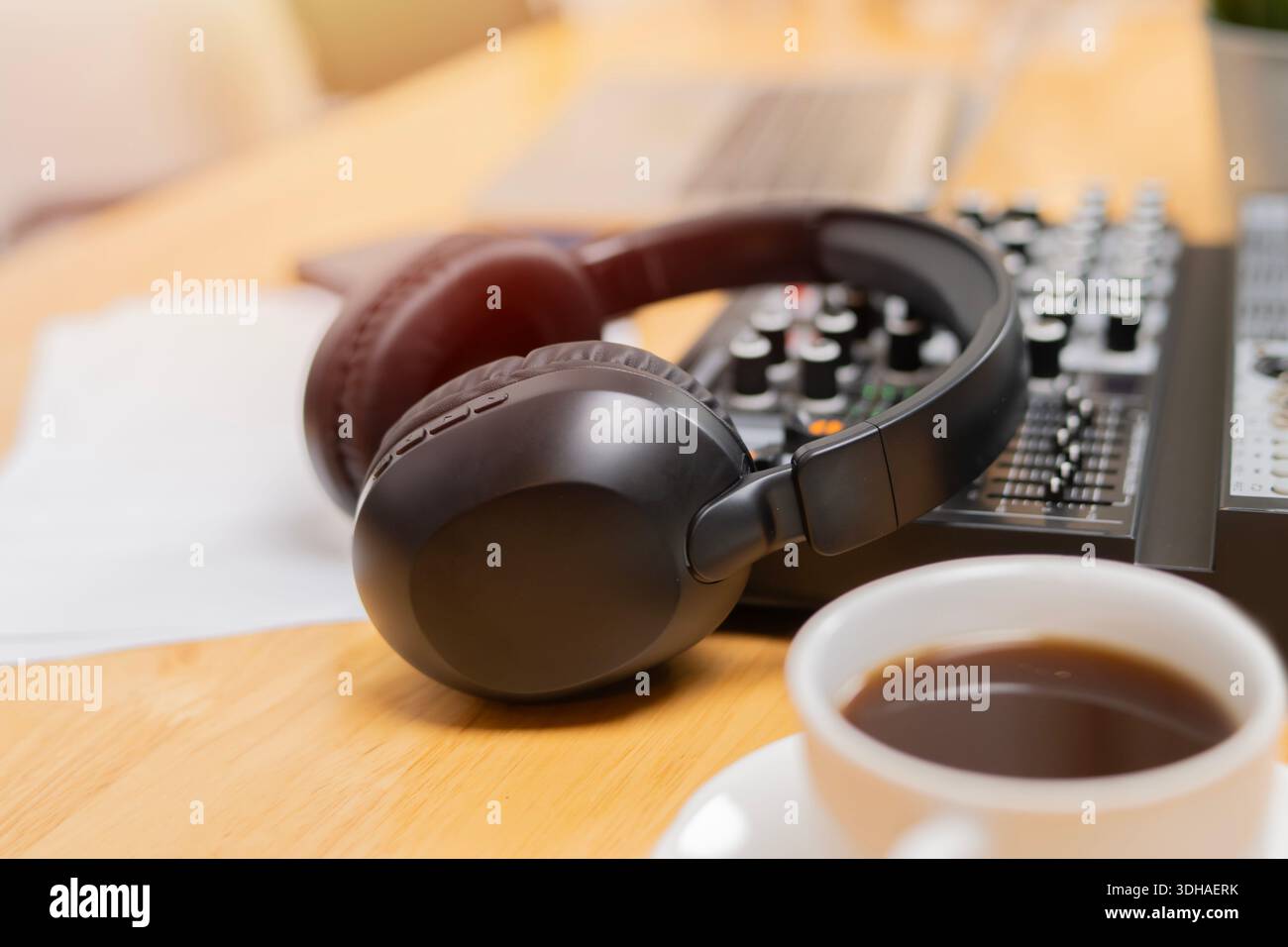Le cuffie si concentrano in modo selettivo su un sistema audio, accanto a una tazza di caffè caldo sulla scrivania. Concetto di impianto audio. Foto Stock