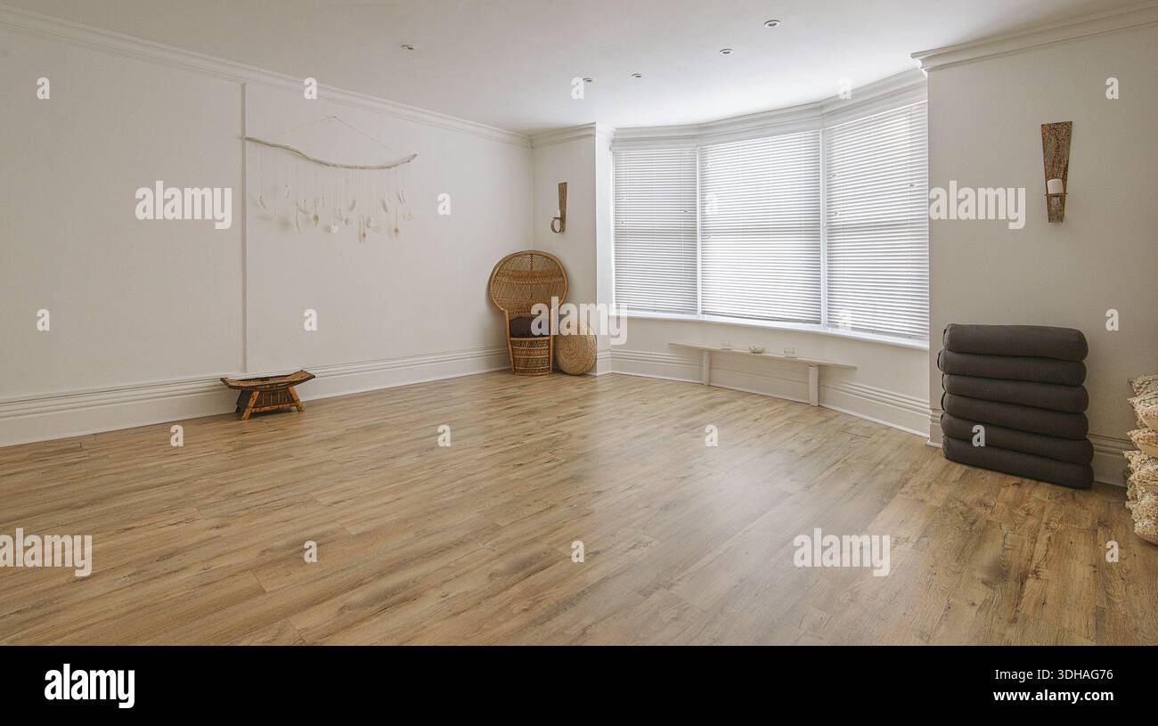 Studio yoga vuoto, spazioso e luminoso, con pavimenti in legno duro, grandi finestre bovindo e oggetti di meditazione ben organizzati. Foto Stock