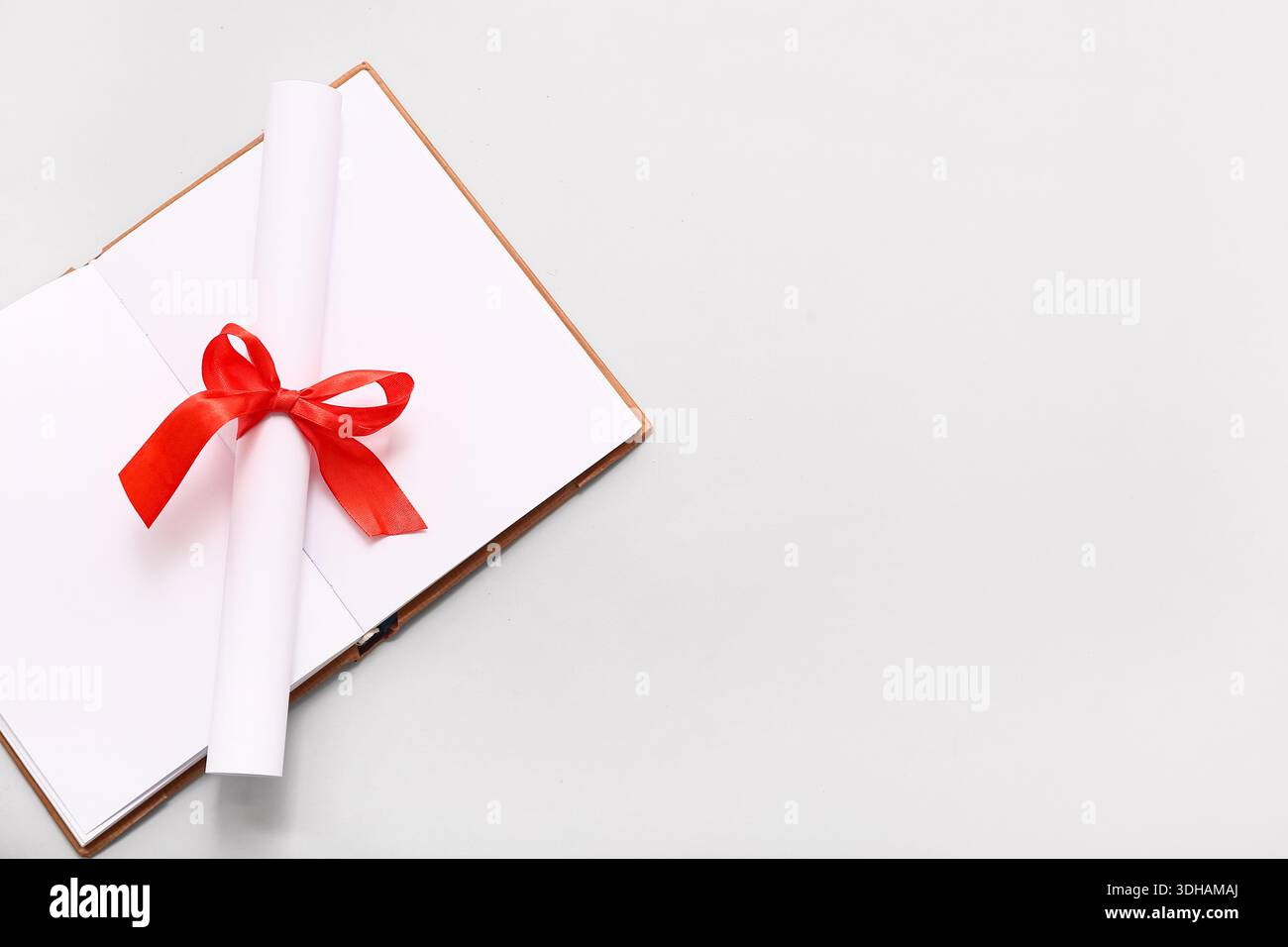 Diploma con nastro rosso e libro aperto su sfondo bianco Foto Stock